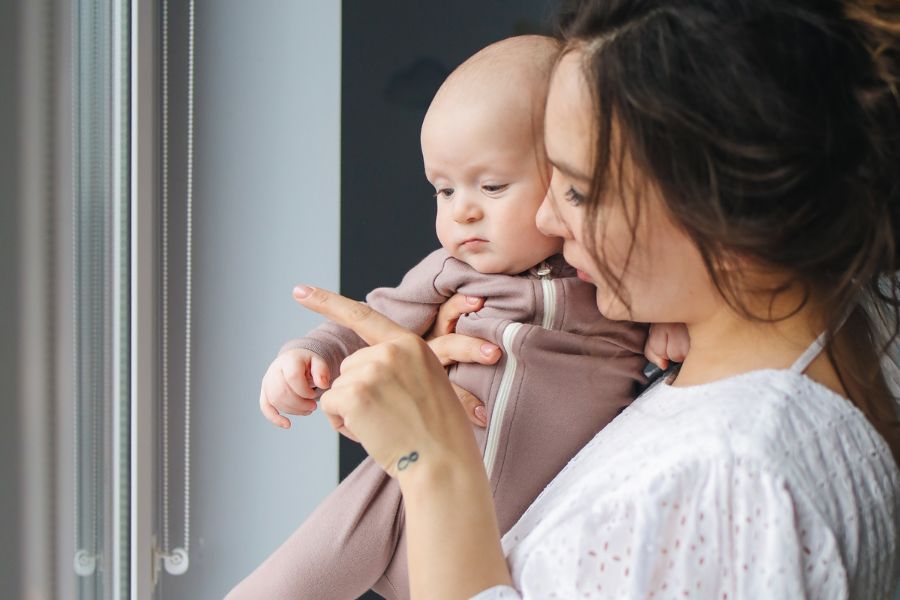 A mother holding her baby looking out the window